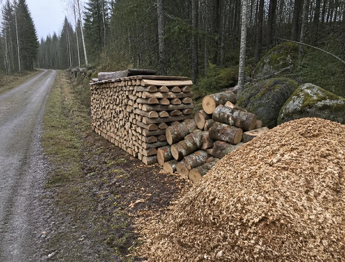 Travad ved och flishög vid skogsväg